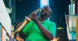 Dans le cadre du &ldquo;Marketing d’influence sans frontières Collaborez avec BaoLiba&rdquo;, un musicien en tee-shirt vert et jeans joue de la saxophone dans le vibrant Times Square. Derrière lui, les écrans lumineux et les bâtiments font de cette scène une illustration de l’ambiance cosmopolite propice aux campagnes d’influence.